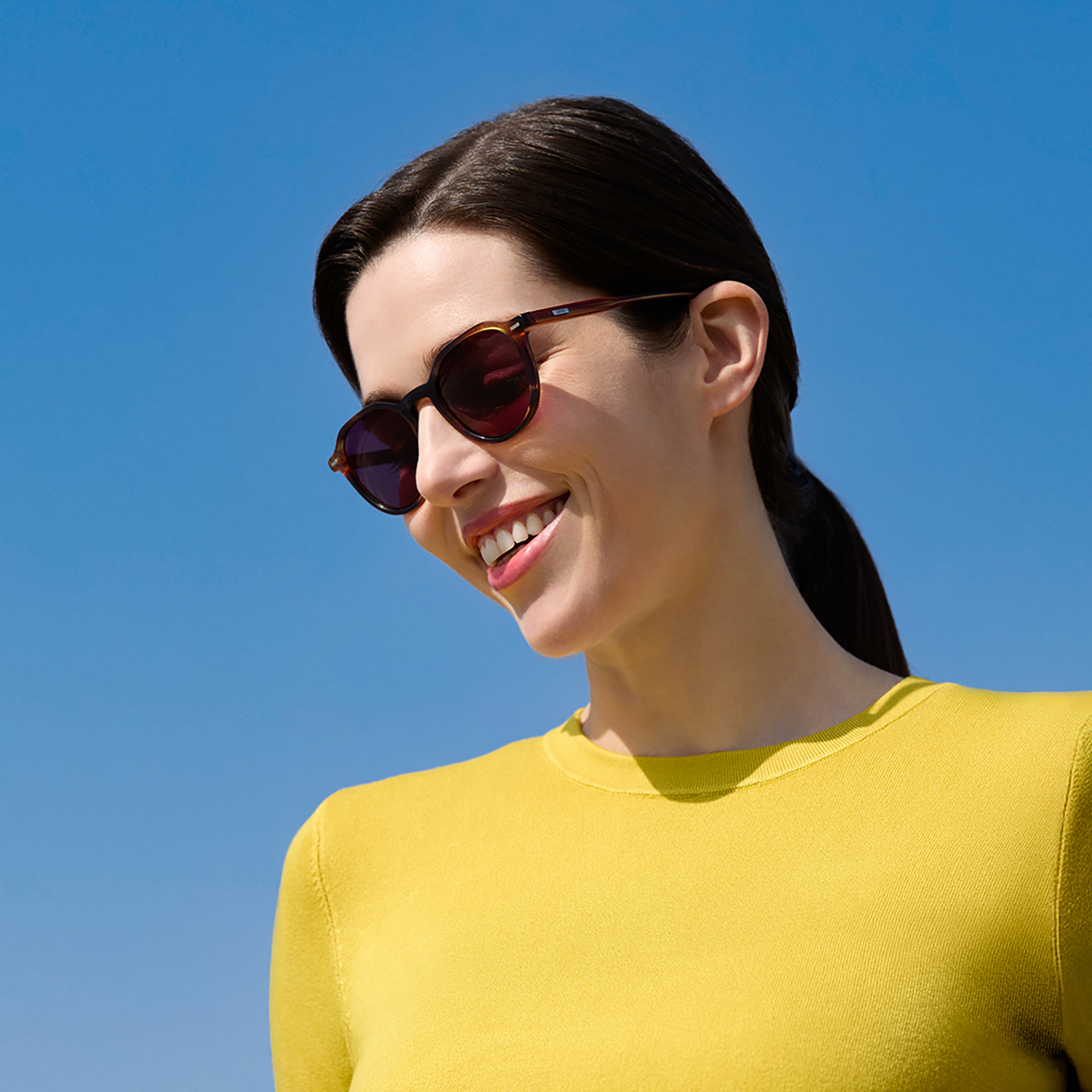 Une femme porte des verres de lunettes de soleil correctrices ZEISS en teinte bordeaux.