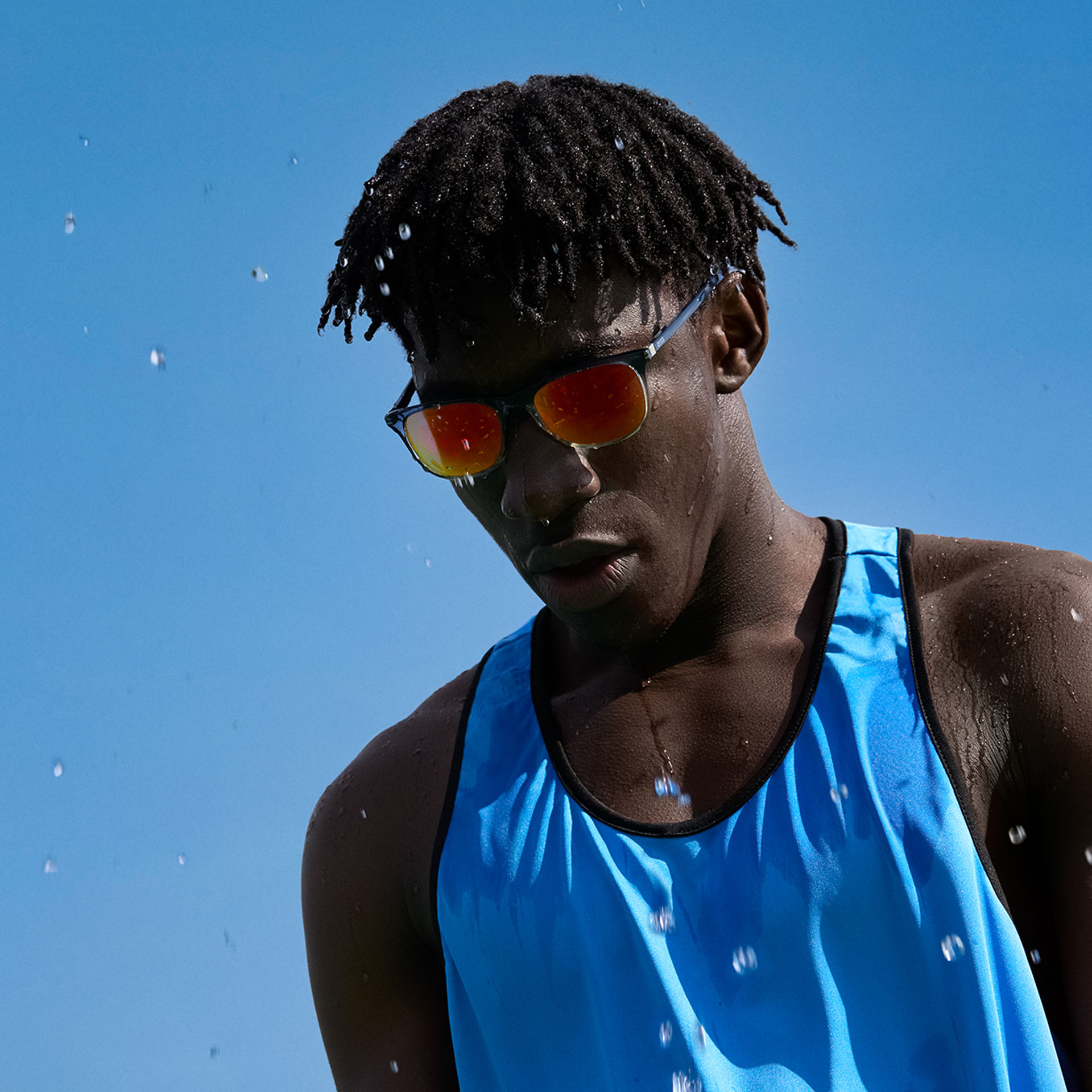 Un jeune homme en tenue de sport et lunettes de soleil ZEISS Performance brun-orange devant un ciel bleu.