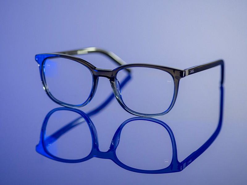 Clear eyeglasses on a blue shiny surface.