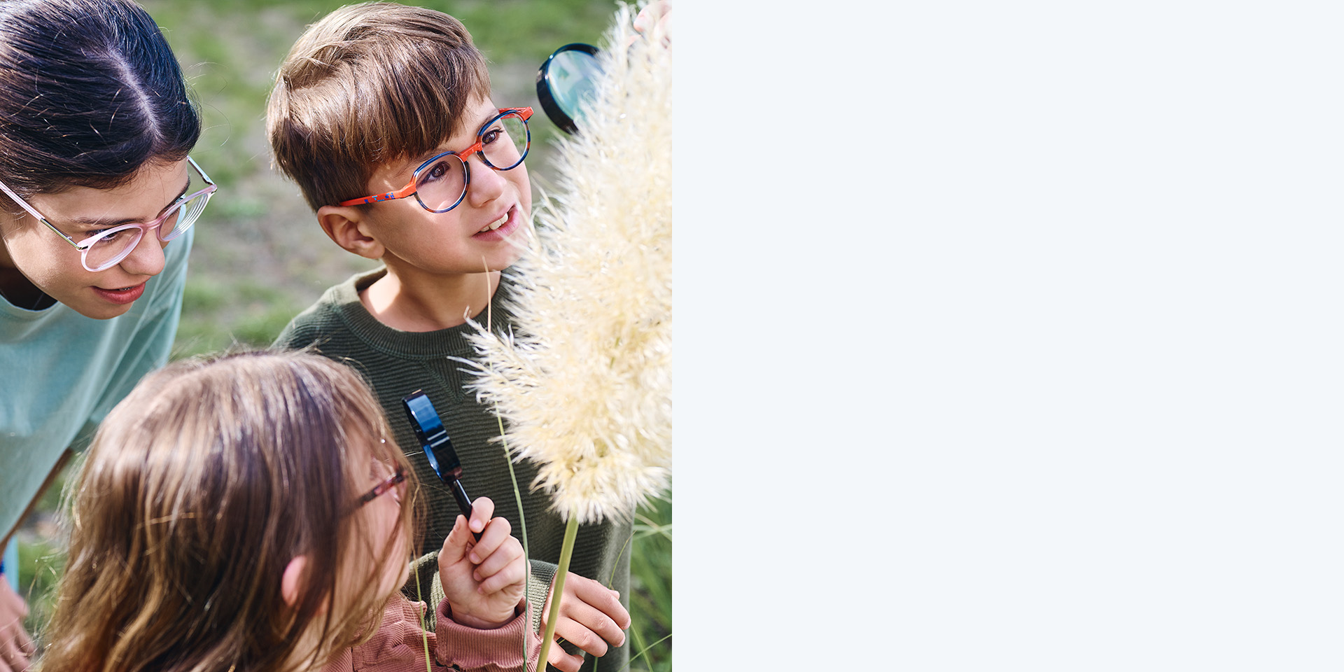 Two girls and one boy wearing ZEISS MyoCare lenses. They are looking at a plant; two of the three kids are looking at the plant through magnifying glasses.
