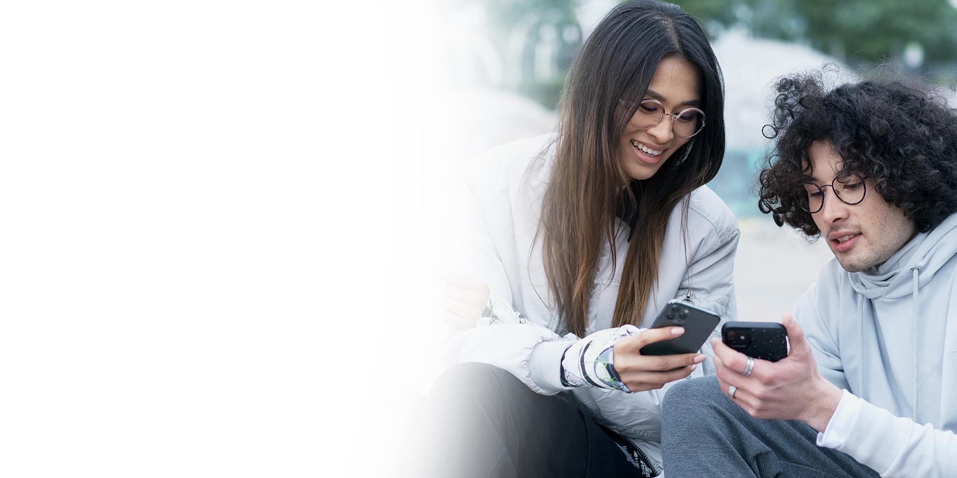 Deux jeunes gens, une femme aux longs cheveux marrons qui sourit et un garçon aux cheveux noirs et bouclés portent des lunettes ZEISS SmartLife et regardent leurs téléphones. 