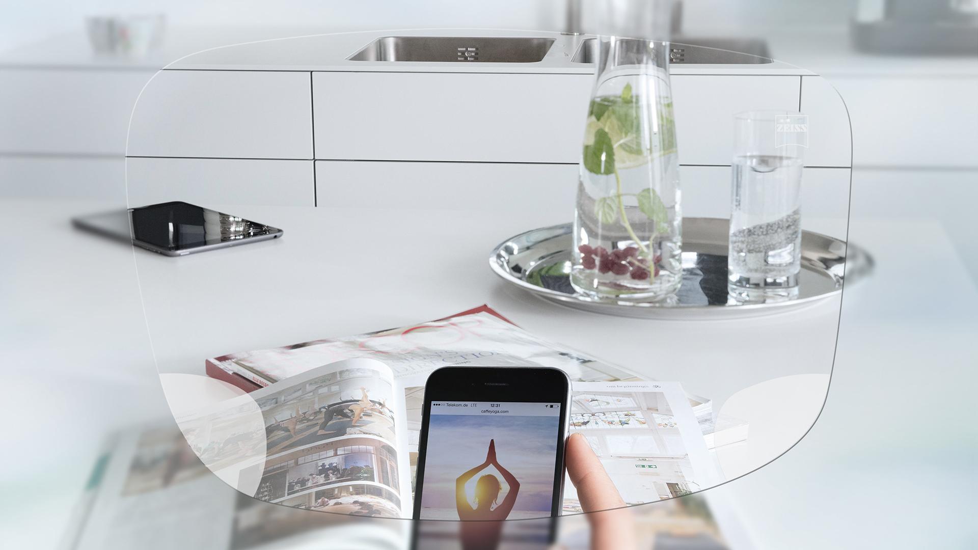 View through ZEISS EnergizeMe Single Vision lens of a smartphone screen and organized kitchen table. 