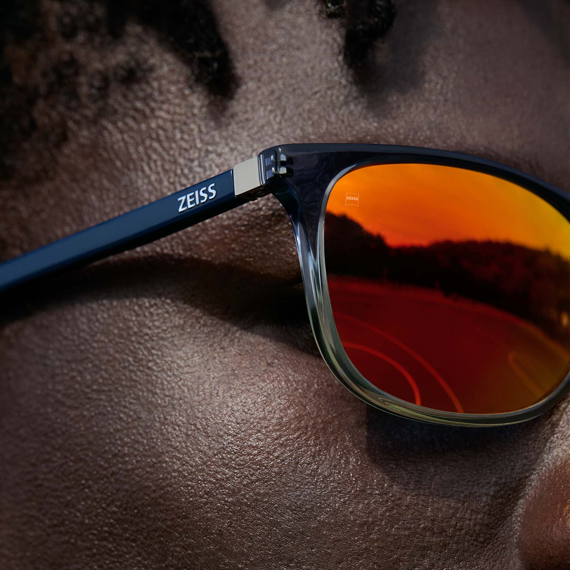 Gros plan d’un homme portant des lunettes ZEISS avec un traitement ZEISS DuraVision Mirror UV en orange.