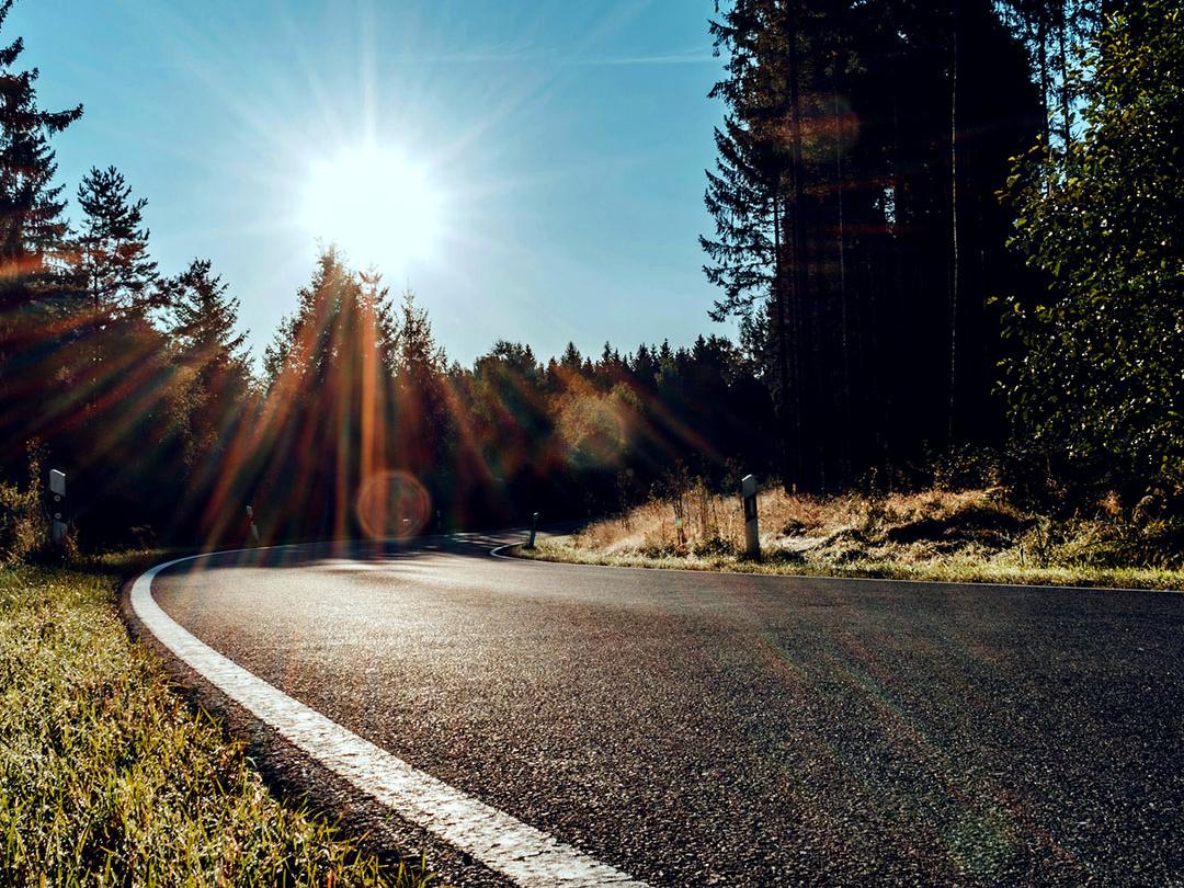 Image coulissante dont la moitié représente une route dans les bois avec une lumière solaire intense, et dont l’autre moitié montre la même route avec un éblouissement réduit et un contraste accru, soulignant l’effet des verres de lunettes de soleil polarisées.