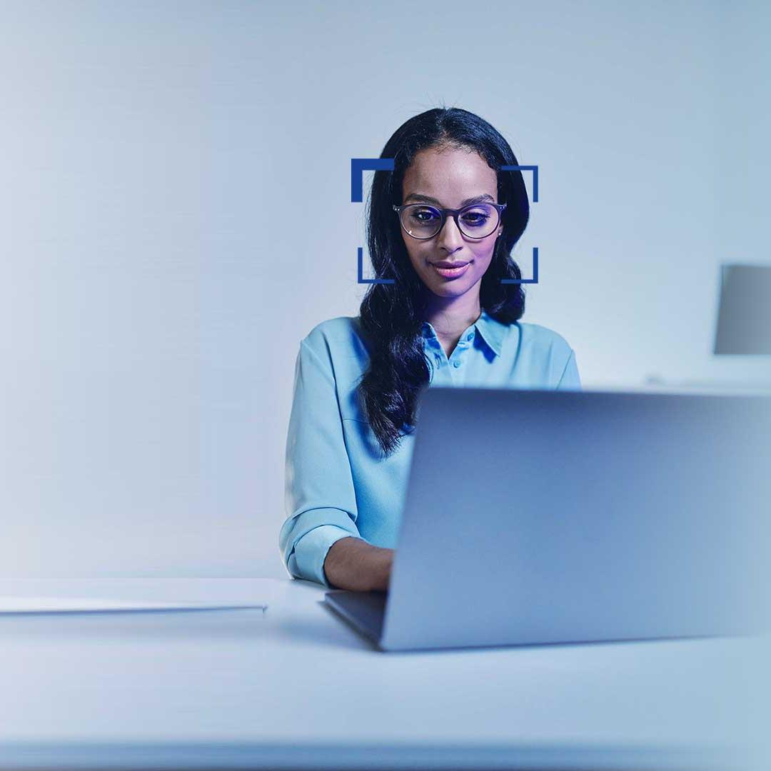 Femme aux cheveux noirs portant des lunettes et souriant devant son ordinateur portable