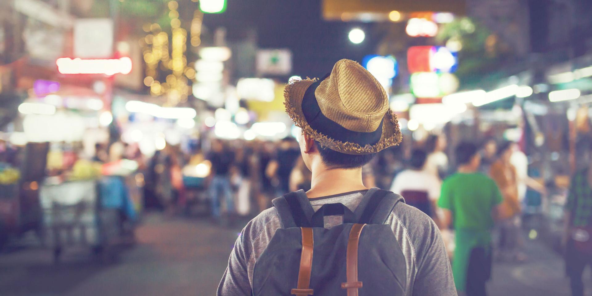 Young Asian traveling backpacker in Khaosan Road night market in evening in Bangkok, Thailand