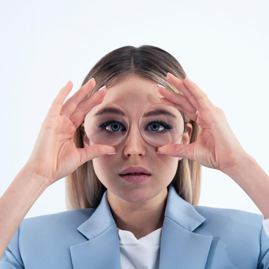 A young woman holding two thick lenses in front of her eyes to show the fish bowl effect.