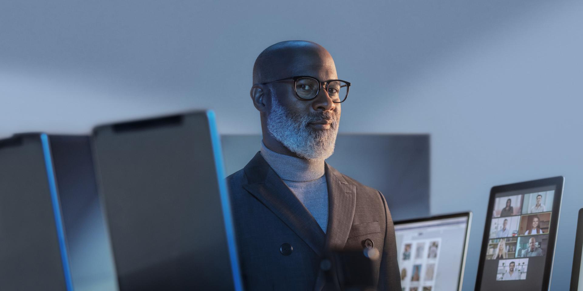 Un homme souriant, entouré d’appareils numériques, qui porte des lunettes ZEISS BlueGuard pour se protéger contre la lumière bleue.