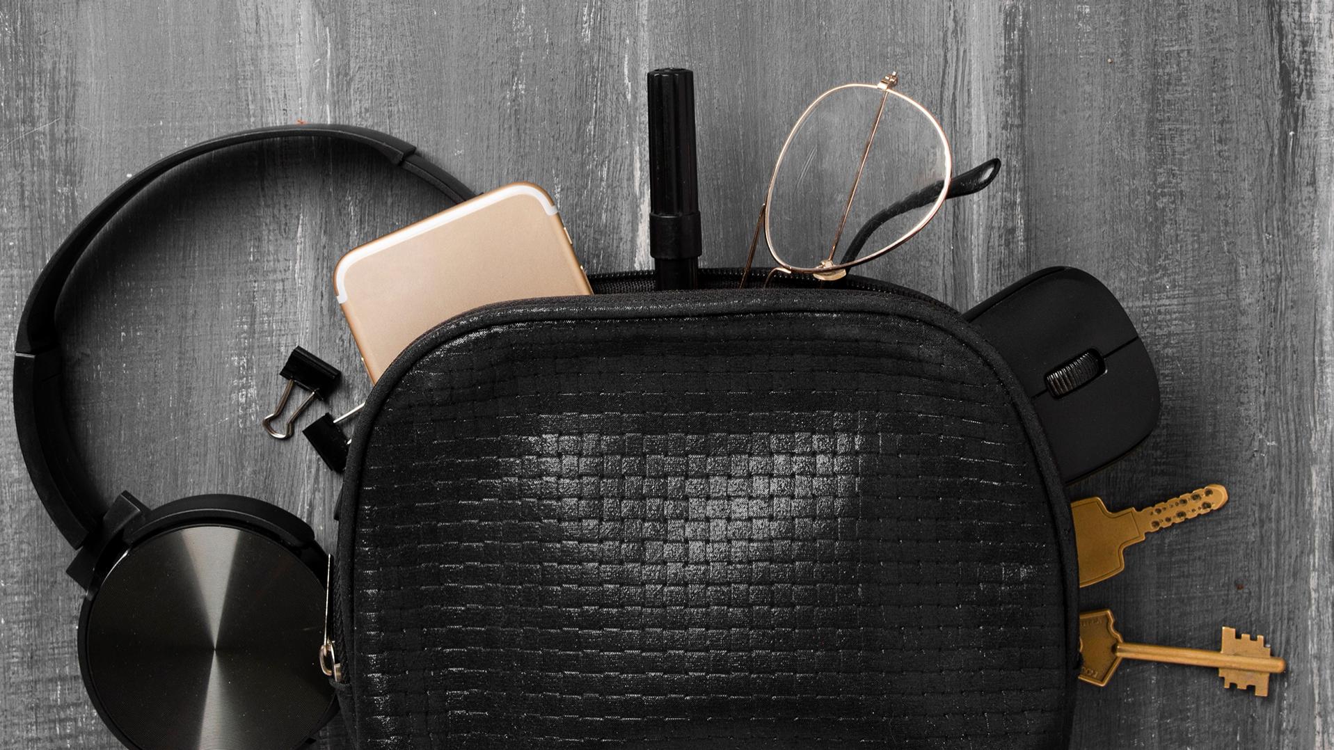 Un petit sac noir d’où sont sortis des écouteurs, un téléphone portable, des clés, des agrafes, un stylo, une souris d’ordinateur et des lunettes équipées de verres ZEISS avec un traitement DuraVision. Ces objets sont maintenant à moitié étalés sur le sol gris.