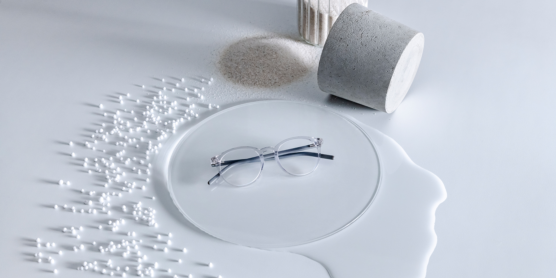 Verres ZEISS dotés d’un traitement DuraVision® placés sur un piédestal en verre entouré d’eau, de sable, de perles et de pierre.