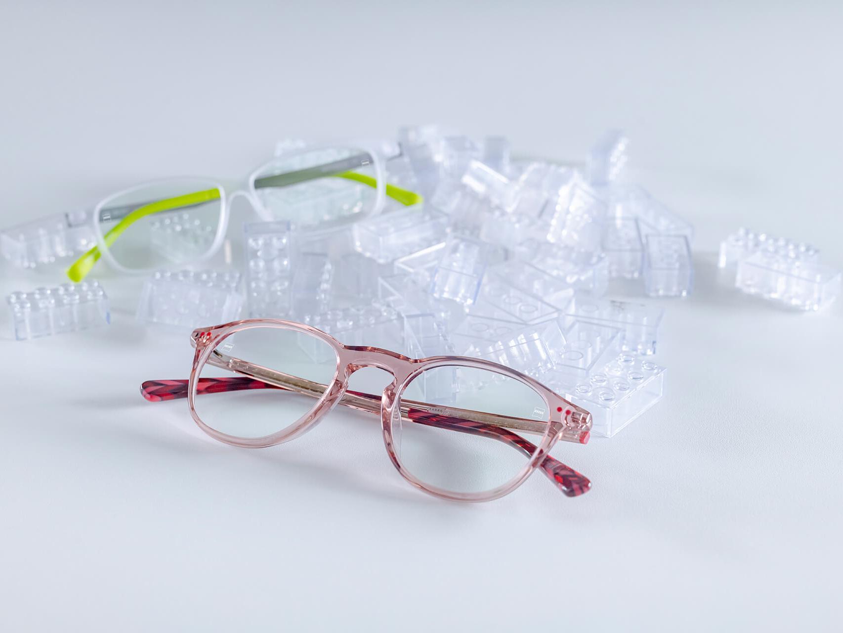 Deux paires de lunettes pour enfants avec des verres ZEISS et le traitement DuraVision® Kids. Les lunettes sont placées entre des briques de construction transparentes pour enfants.
