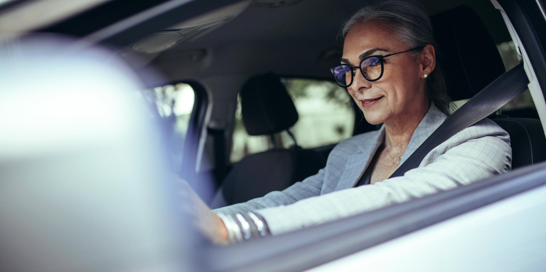 Une femme d’âge mûr dans une voiture porte des lunettes avec des verres ZEISS DriveSafe.
