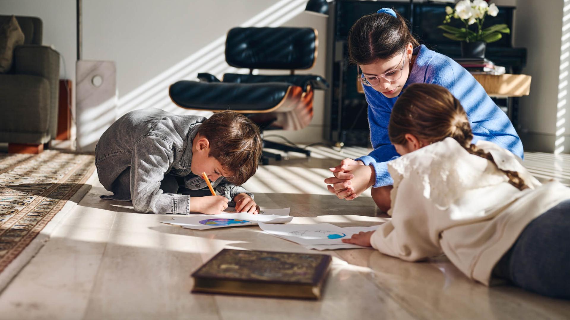 Des enfants en train de dessiner sur le sol, les yeux proches de la feuille. 