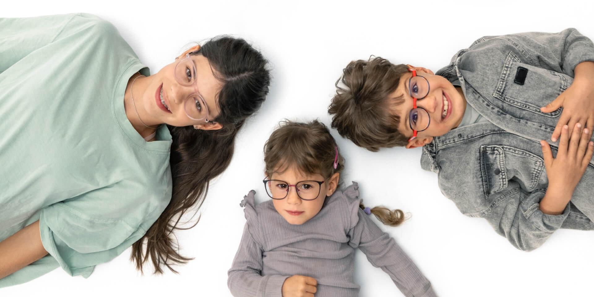 Un adolescent et deux jeunes enfants portant des verres ZEISS dédiés à la myopie évolutive sont couchés au sol.
