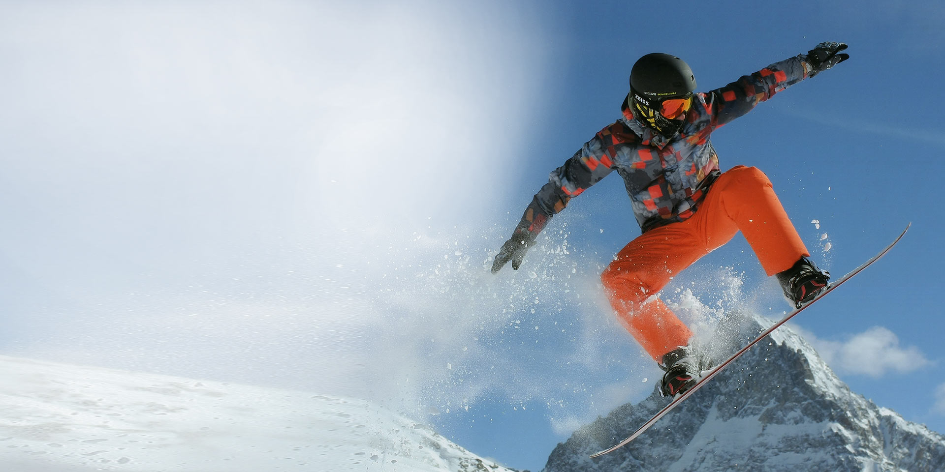 A man jumping with a snowboard. For protection, he is wearing a black ski helmet and ZEISS snow goggles with Interchargeable technology.