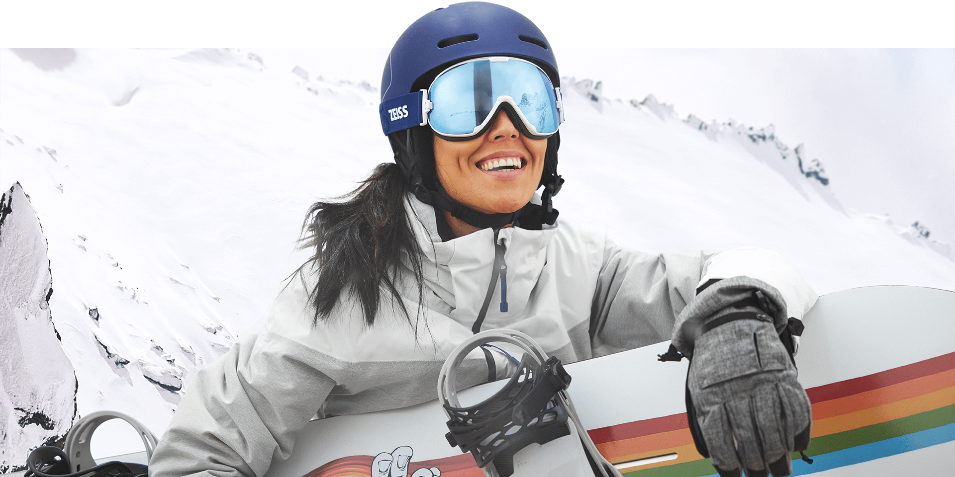 Une jeune femme portant des lunettes de neige dotées de la technologie interchangeable de ZEISS et tenant un snowboard.
