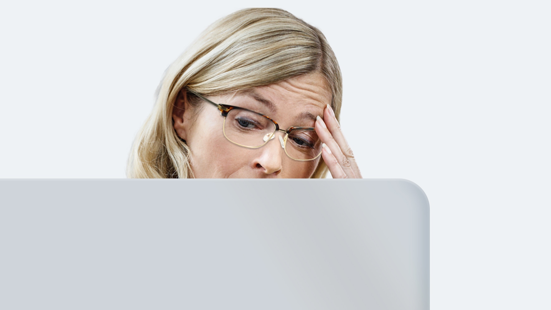A middle-aged woman with long blonde hair wearing distance glasses is experiencing eyestrain because her lenses are not made for staring at a screen all day.