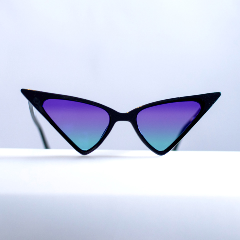 Extraordinary cat-eye sunglasses on a white surface with cyan-purple gradient tint